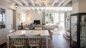 Een ruime woonkamer met een groot raam, een open haard en een eethoek met een witte tafel en stoelen.