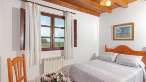 Ein Schlafzimmer mit Holz-Kopfteil, einem Bett mit gemusterten Betttextilien, einem Fenster mit Vorhängen, einem Heizkörper und einem gerahmten Bild an der Wand.