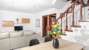 Ein Wohnzimmer mit einer Couch, einem Esstisch, einem Fernseher und einer Treppe.