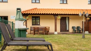 Ein Gebäude mit einem Ziegeldach, einer Terrasse mit Tisch und Stühlen sowie einem begrünten Außenbereich.