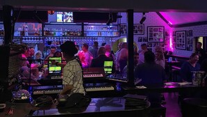 Eine Bar mit DJ-Pult, Flaschenregalen und Gästen.