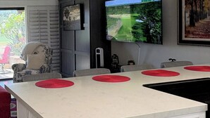Eine moderne Küche mit einer großen Kochinsel, einem an der Wand montierten Flachbildfernseher und einem Essbereich mit grauen Stühlen.