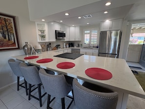 A modern kitchen with white cabinets, a stainless steel refrigerator, and a central island with bar stools. - Desert Blossom House @ The Resort 10th hole
 (Palm Desert)