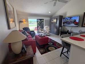 A living room with a sofa, armchair, and a TV on the wall. - Desert Blossom House @ The Resort 10th hole
 (Palm Desert)