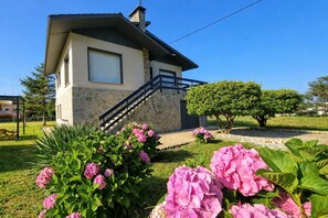 A two-story house with a stone facade, a visible staircase, and a well-maintained garden with pink flowers. - Villa Mauro Vivienda Vacacional (Naves (Posada Llanes))