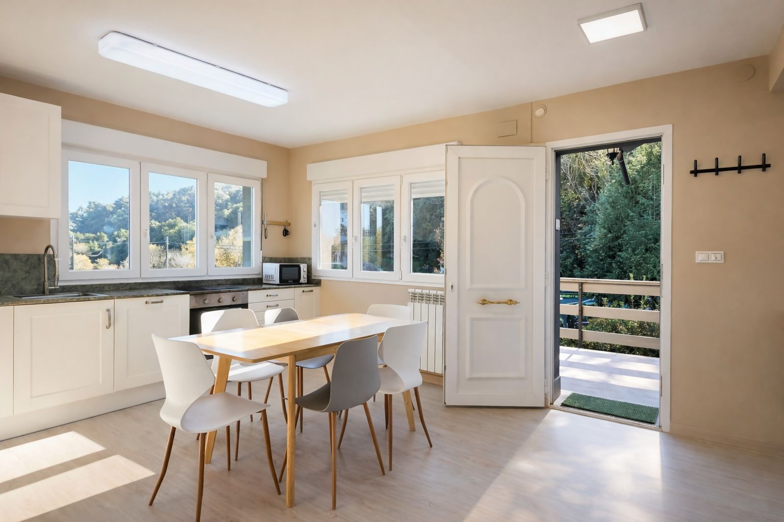 A modern kitchen with white cabinets, a dining table with chairs, and a view of greenery outside.