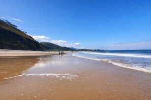 A beach with a clear sky, sandy shore, and a few people walking. - Villa Mauro Vivienda Vacacional (Naves (Posada Llanes))