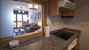 Une cuisine moderne dotée de plans de travail en granit, d’une cuisinière encastrée et d’un four à micro-ondes. Un coin repas est visible à travers une cloison en verre et comprend un canapé et une table.