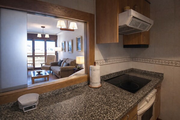 Una cocina moderna con encimeras de granito, estufa integrada y microondas. Se observa un área de comedor a través de una partición de vidrio, con un sofá y una mesa.
