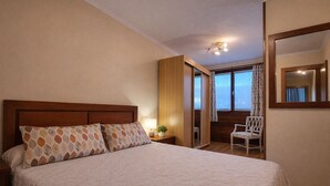 A bedroom with a large bed, a nightstand, a chair, and a view through a door.