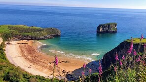 A coastal landscape with a sandy beach, rocky cliffs, and clear blue sea.