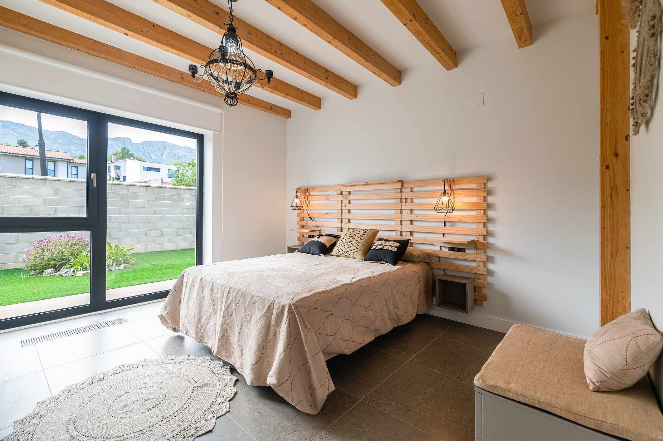 A bedroom with a bed, a bench, a large window, and a view of the outdoors.