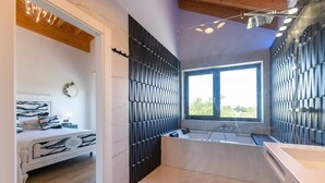 A modern bathroom with a large bathtub, a window, and a shower area. - Villa Vacacional La Raizona (Pancar)