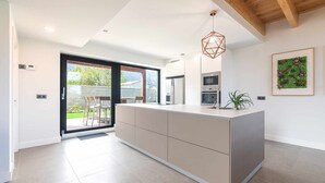 A modern kitchen with a large island, built-in appliances, and a sliding glass door to a patio. - Villa Vacacional La Raizona (Pancar)