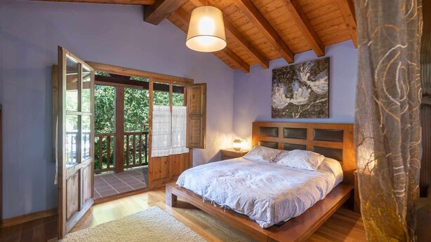 A bedroom with a wooden bed, a large window, and a ceiling light. - Villa Las Ardillas con Piscina (Cardoso (Llanes))