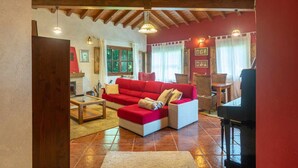 A cozy living room with a red sofa, wooden coffee table, and a dining area with wicker chairs. - Villa Las Ardillas con Piscina (Cardoso (Llanes))