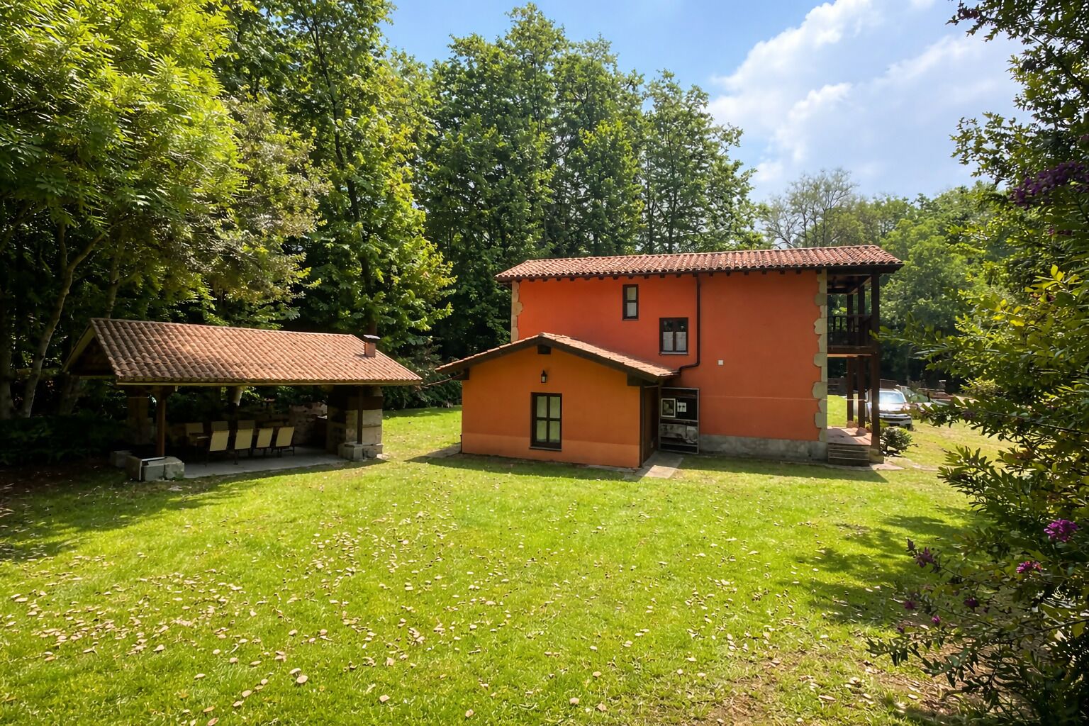 A two-story building with a red roof and orange walls, surrounded by a grassy lawn and trees.