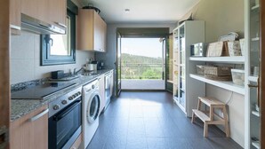 Une cuisine compacte équipée d’un lave-linge, d’une cuisinière et d’un évier. Un balcon offre une vue sur la verdure.
