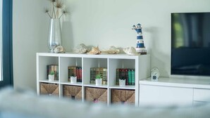 Un meuble de rangement blanc, destiné à accueillir des objets de décoration, avec des livres, des coquillages décoratifs et une maquette de phare.