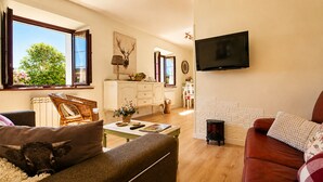 A living room with a sofa, a red armchair, a television, a fireplace, and a dining area with a table and chairs. - Casa La Venta de Pedro (Ribadesella)