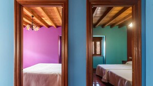 Corredor que leva a dois quartos com tetos de madeira e uma janela com cortinas estampadas.