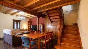 Uma sala de estar ampla com escada de madeira, um sofá, uma mesa de jantar com cadeiras e uma televisão.
