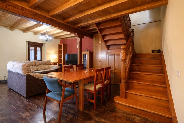 A spacious living area with a wooden staircase, a sofa, a dining table with chairs, and a television.