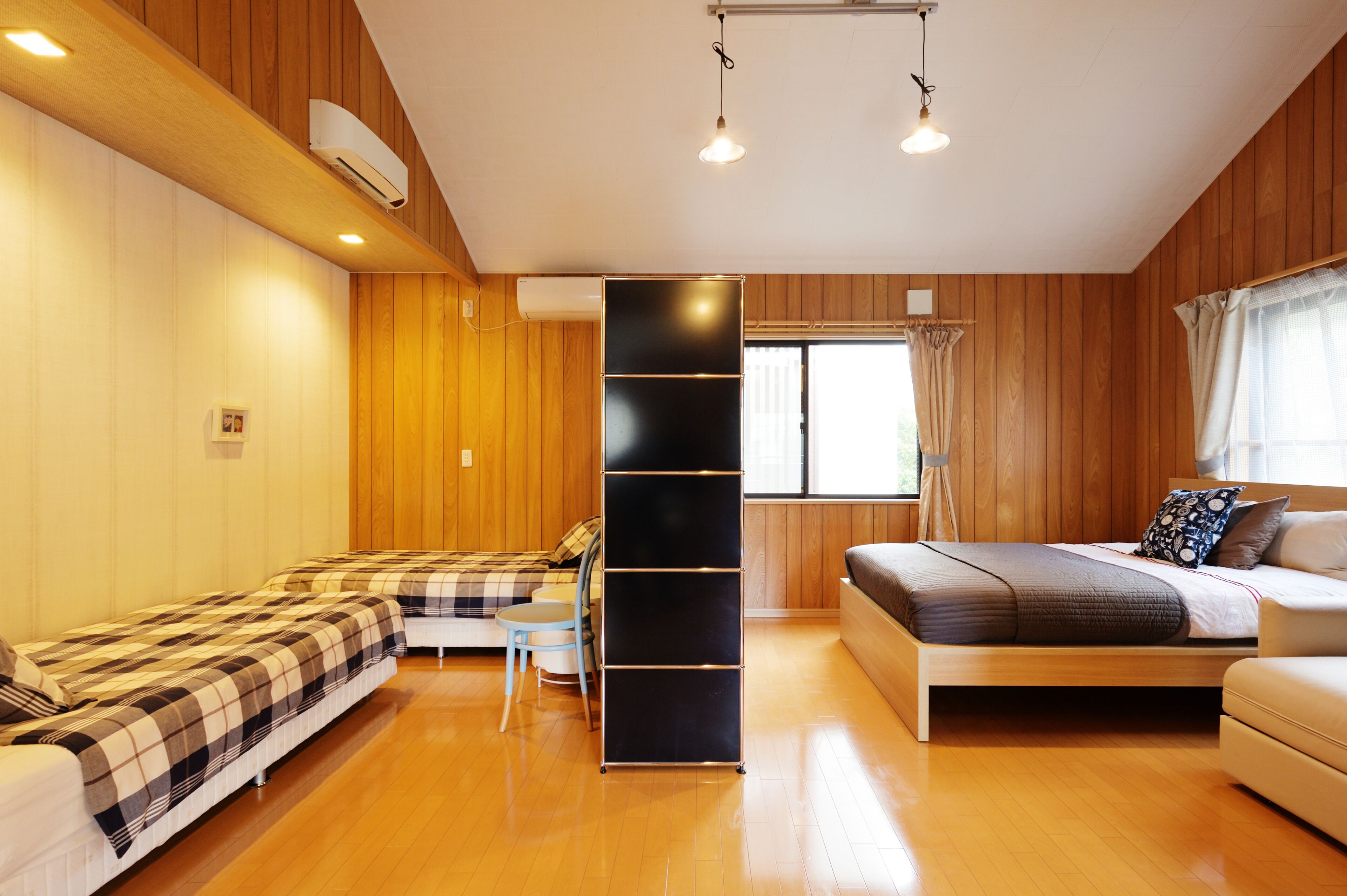 A room with wooden panel walls, a bed, a sofa, a small table, and a black shelving unit.