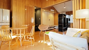 A modern interior with wooden paneling, a dining area with chairs and a table, a sofa, and a bed. - SAYA Suite Kishinosato Annex (Osaka)