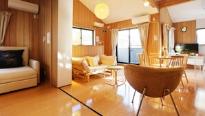 A spacious room with a wooden floor, a sofa, a dining table, and a large window. - SAYA Suite Kishinosato Annex (Osaka)