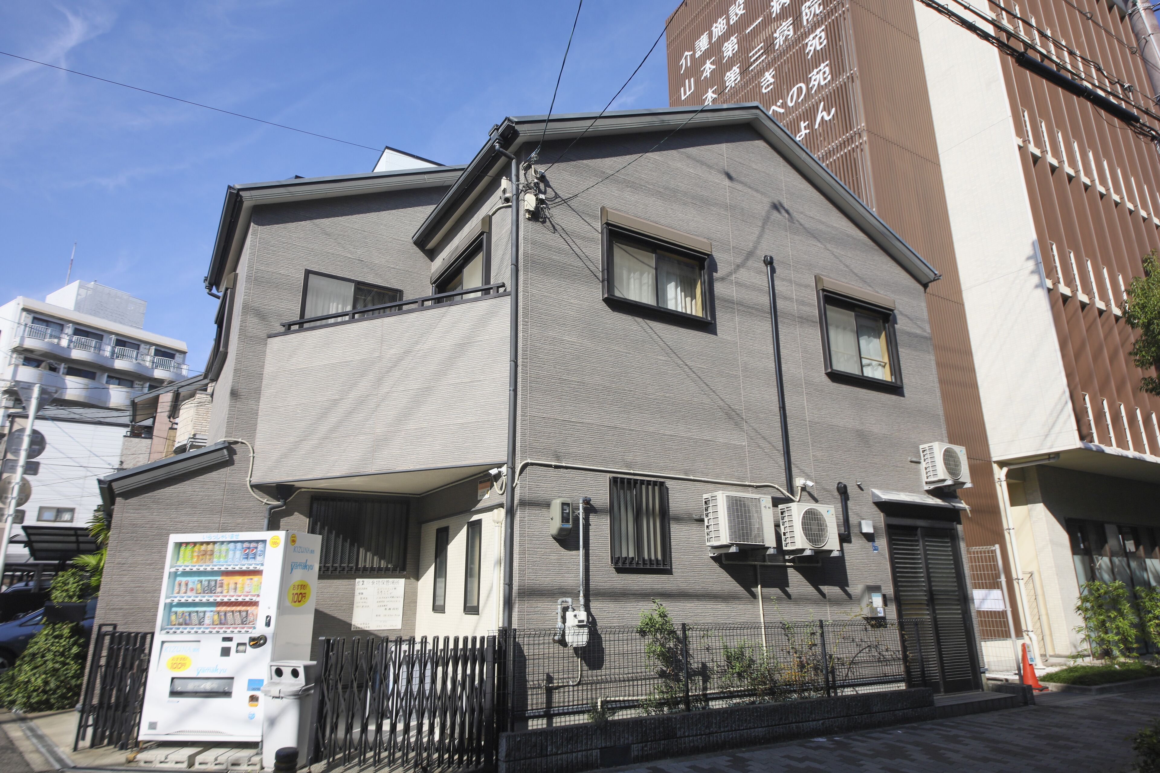 Un edificio residencial de dos pisos con máquina expendedora y unidades de aire acondicionado en el exterior.