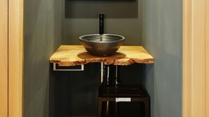 A narrow hallway with a wooden bench, a black sink, and a mirror on the wall. - SAYA Suite Kishinosato Annex (Osaka)