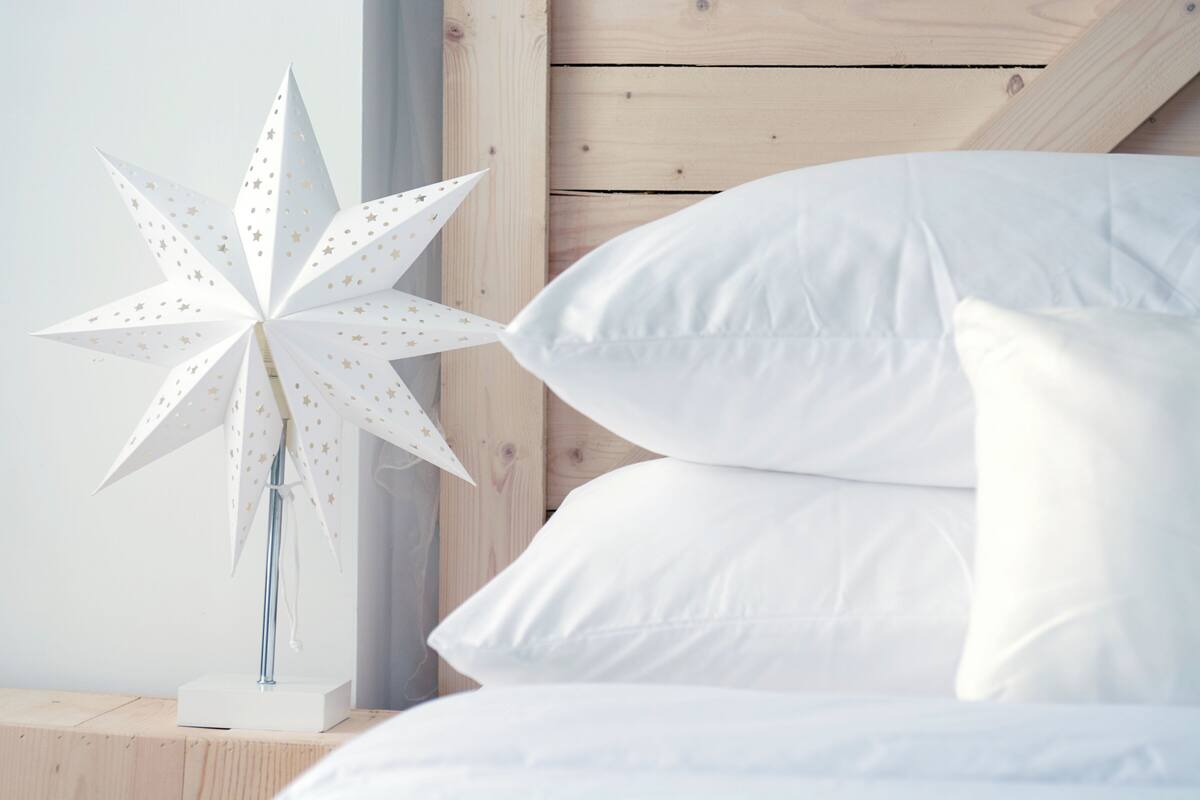 A bed with white pillows and a white star-shaped paper lantern on a wooden nightstand.