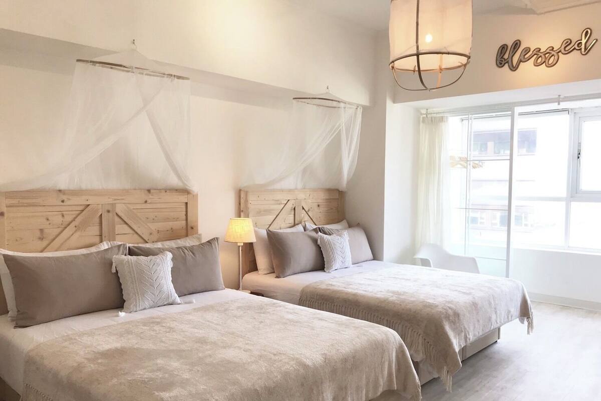A hotel room with two beds, a wooden headboard, a bedside lamp, and a window with a view.