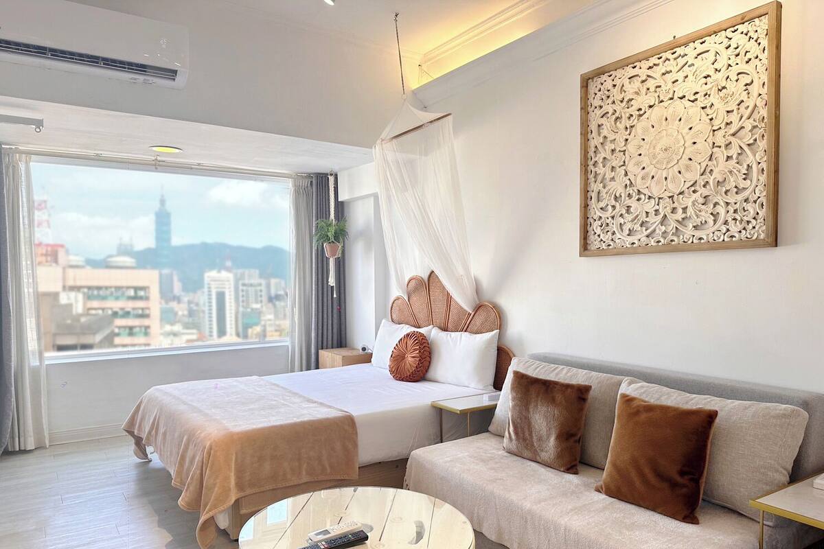 A modern hotel room with a large bed, a sofa, a round coffee table, and a city view.