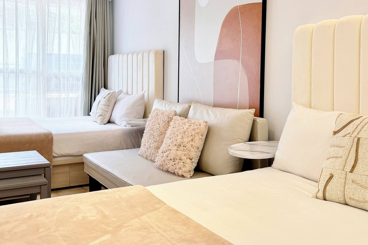 A hotel room with a large bed, a smaller sofa, a bedside table, and a window with curtains.
