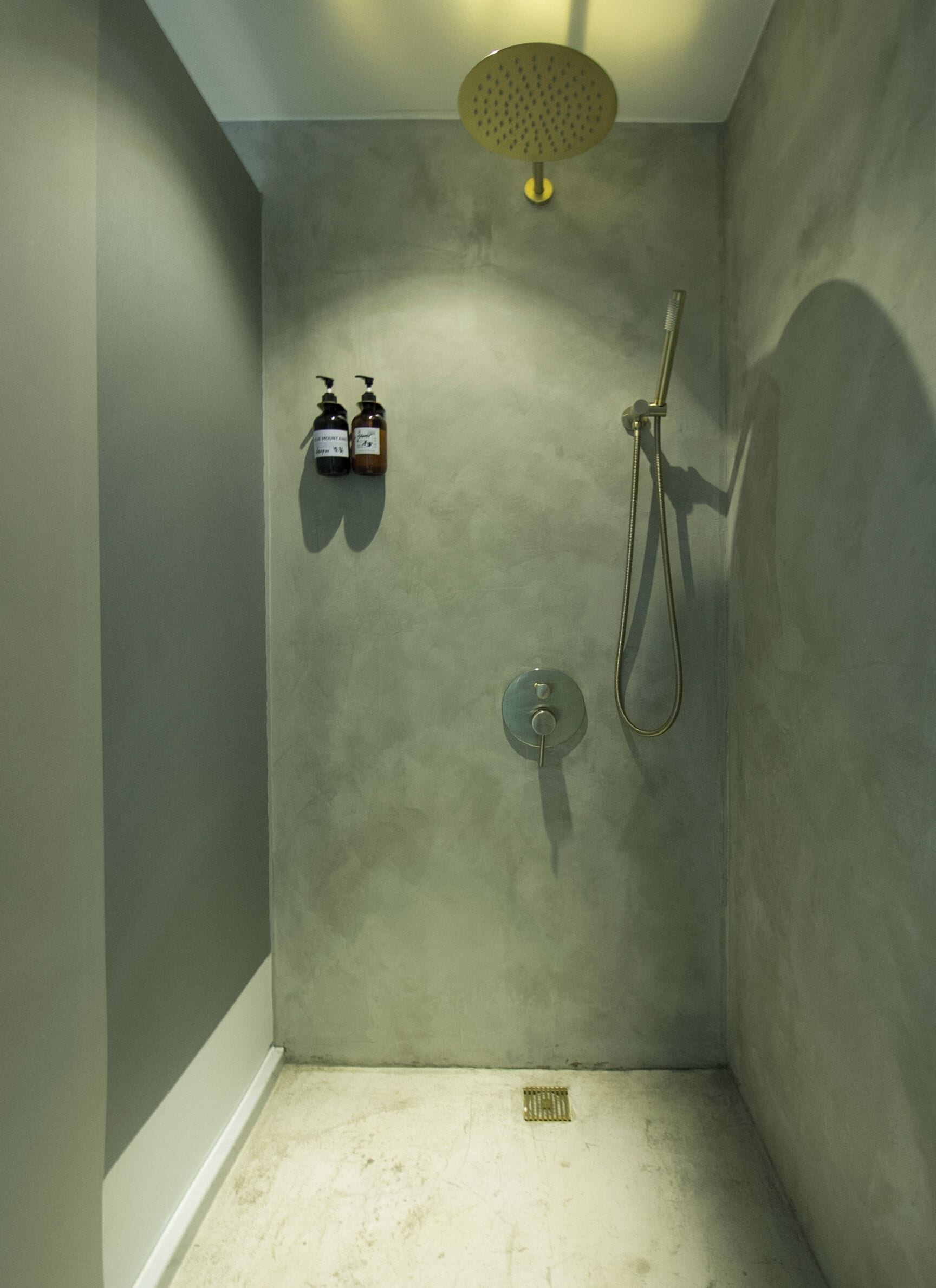 A small, enclosed shower area with a handheld showerhead, a handheld shower nozzle, and two bottles of shampoo and conditioner on the wall.