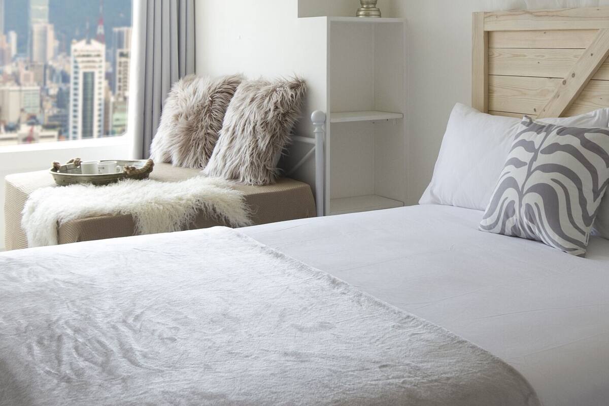 A bedroom with a large bed, a view of a cityscape, a wooden headboard, and a bedside table with a tray.