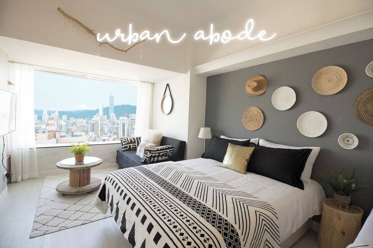A modern bedroom with a city view, a bed with patterned bedding, a round side table, and decorative wall art.