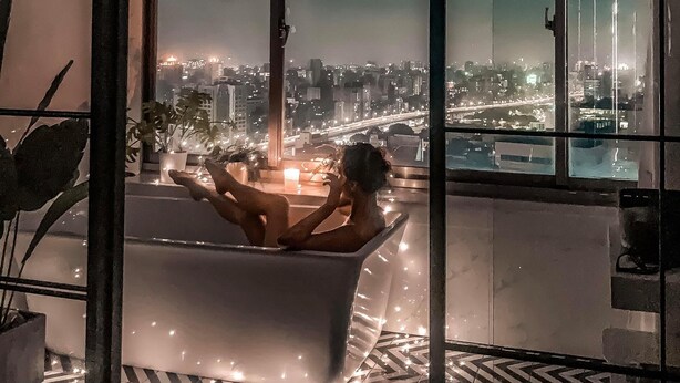 A modern bathroom with a bathtub, large windows, and a city view. - Urban Abode Apartment 1 (Taipei)