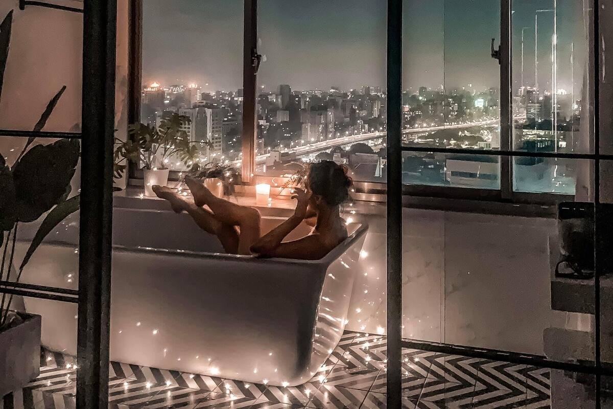A modern bathroom with a bathtub, large windows, and a city view.