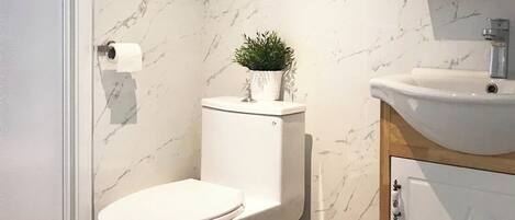 A modern bathroom with a toilet, sink, and shower. There are shelves above the toilet and sink, and a mirror above the sink.