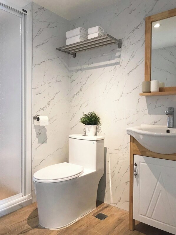 A modern bathroom with a toilet, sink, and shower. There are shelves above the toilet and sink, and a mirror above the sink.