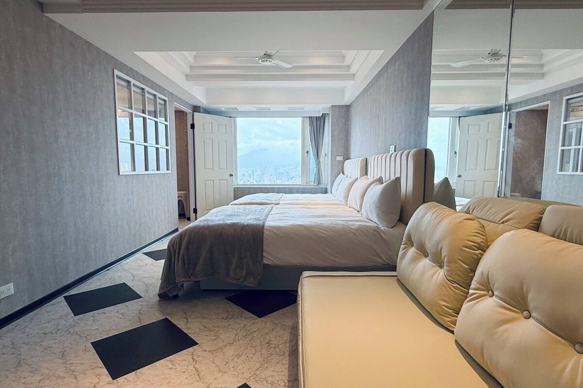 A modern hotel room with a large bed, a sofa, and a city view through the window.