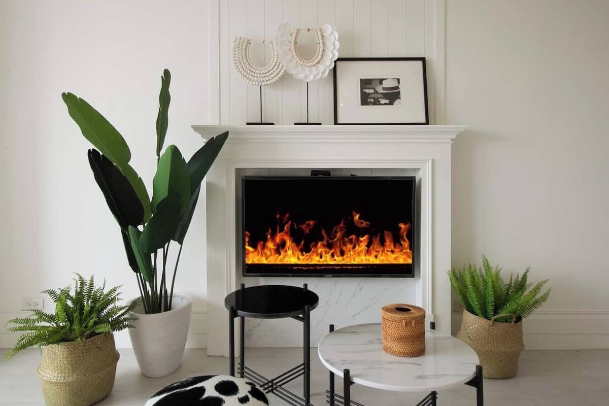 A living room with a fireplace, a round table, and potted plants.
