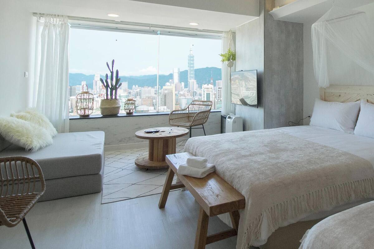 A hotel room with a large bed, a sofa, a small table, and a view of the cityscape.