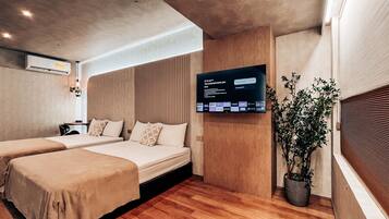 A hotel room with two beds, a TV mounted on the wall, a potted plant, and a wooden headboard.