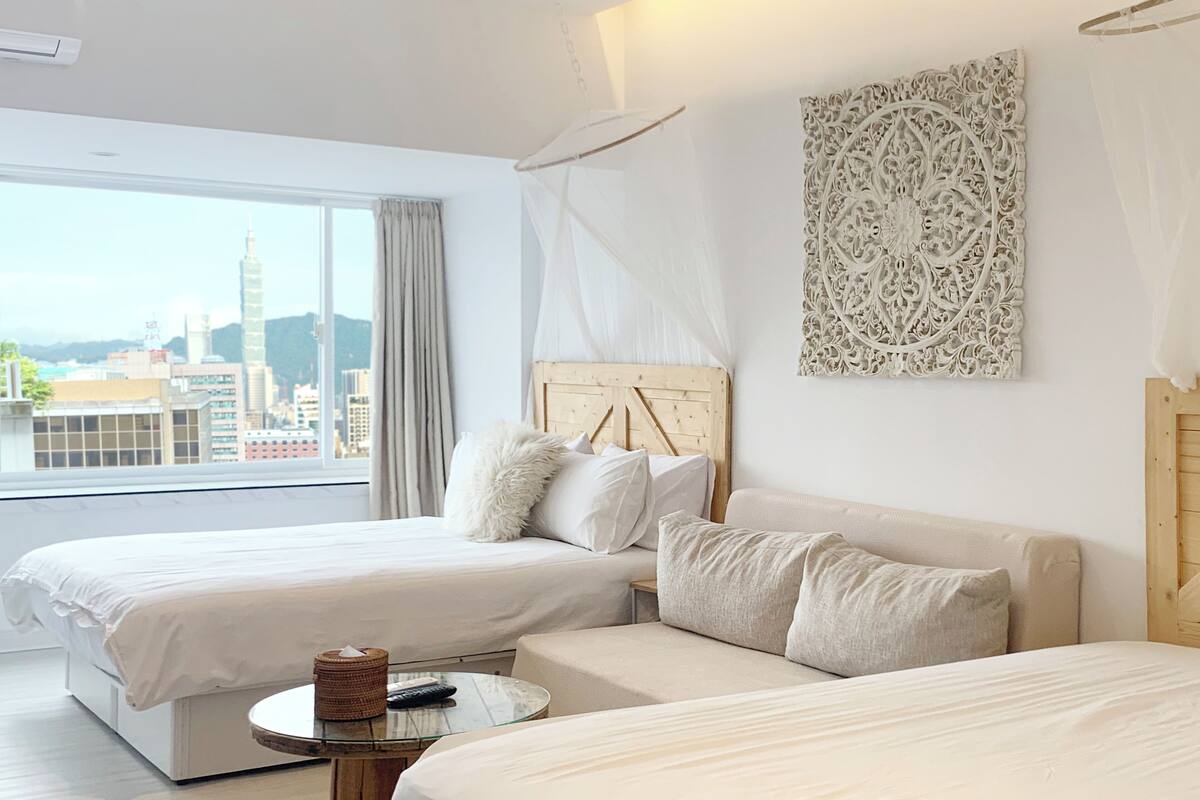 A hotel room with two beds, a small round table, and a view of the cityscape.