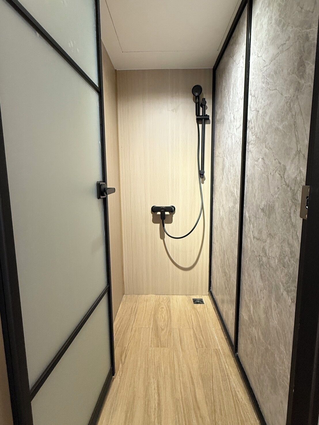 A walk-in shower with a wooden floor and a marble wall.
