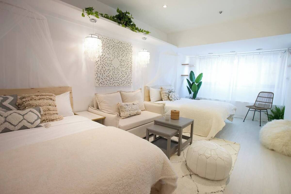 A modern bedroom with two beds, a sofa, a small table, and a chair.